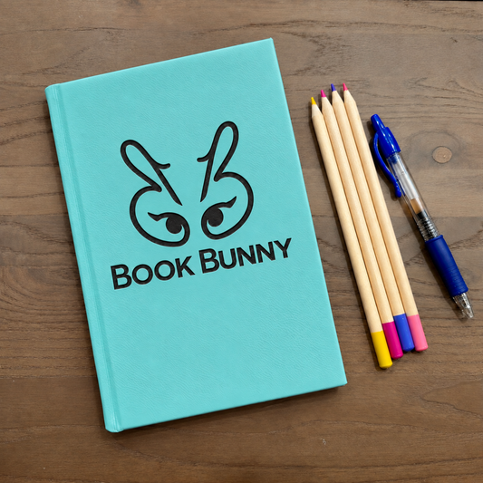 A turquoise hardcover notebook with a black bunny graphic and the text 'BOOK BUNNY' on the cover, placed on a wooden surface next to four wooden pencils and a blue pen.