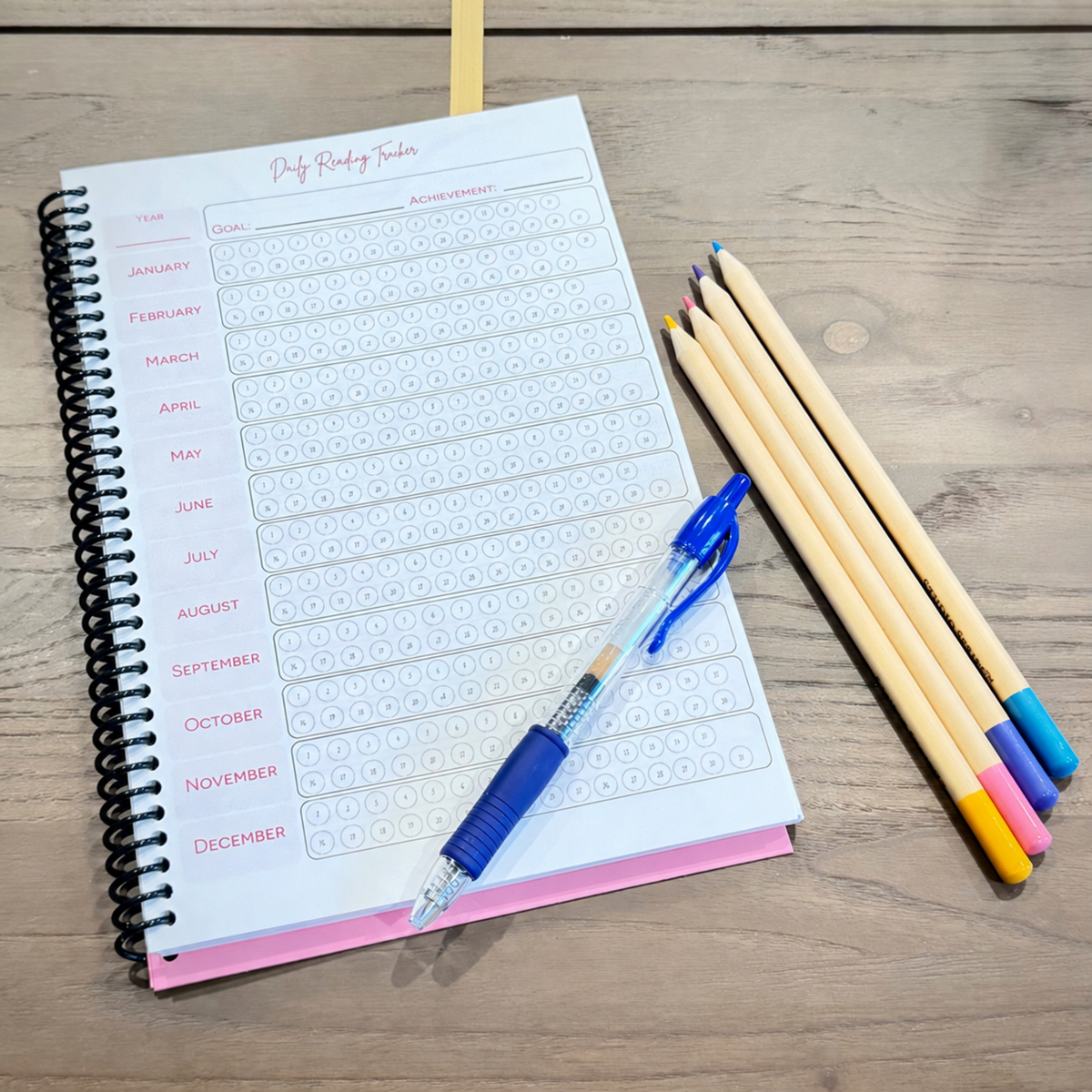 Daily Reading Tracker inside the pink Book Bunny™ Official Quick Review Book Journal, shown with a blue pen and colored pencils.