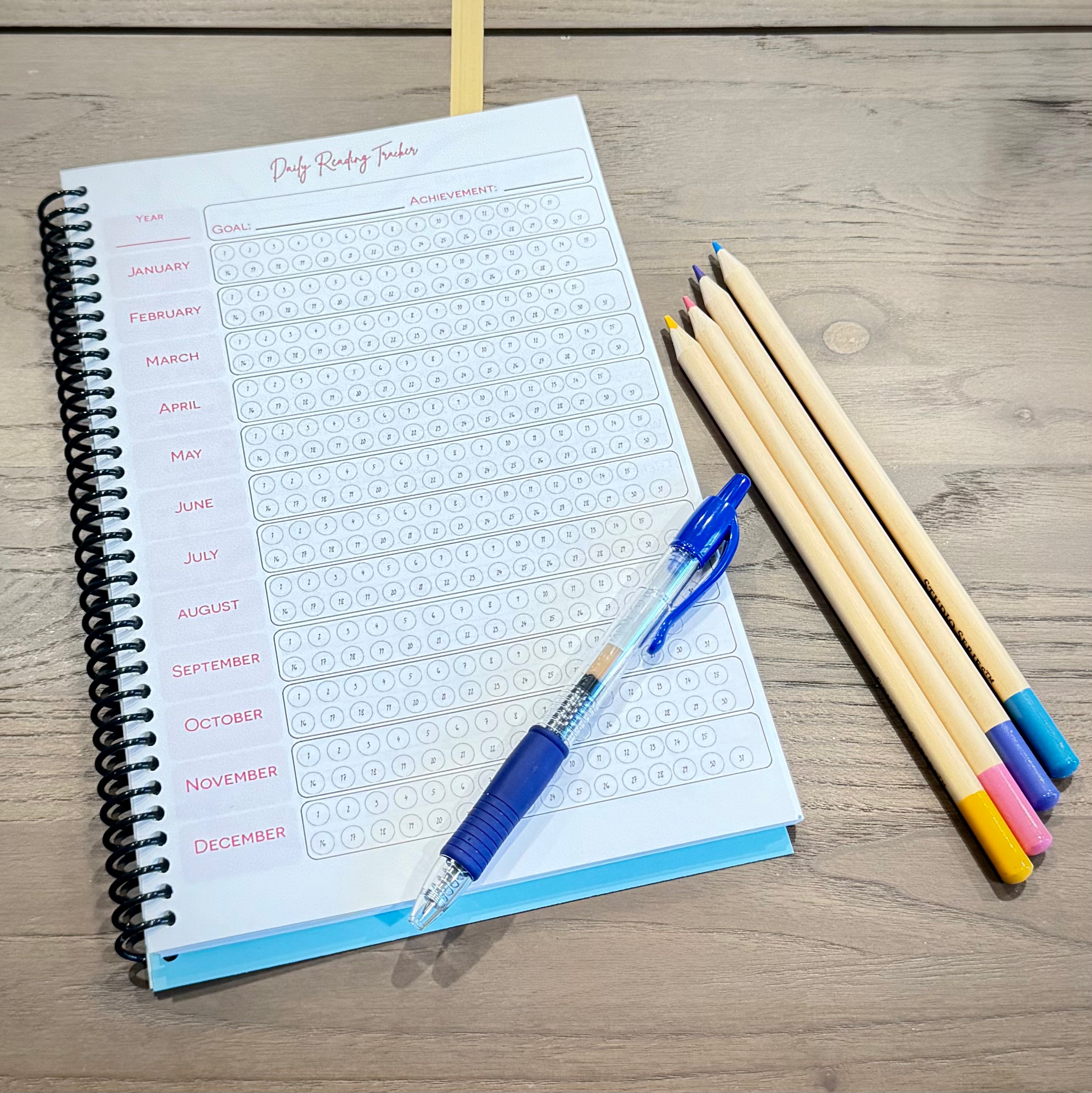 Daily Reading Tracker inside the Book Bunny™ audiobook journal, shown with a blue pen and colored pencils