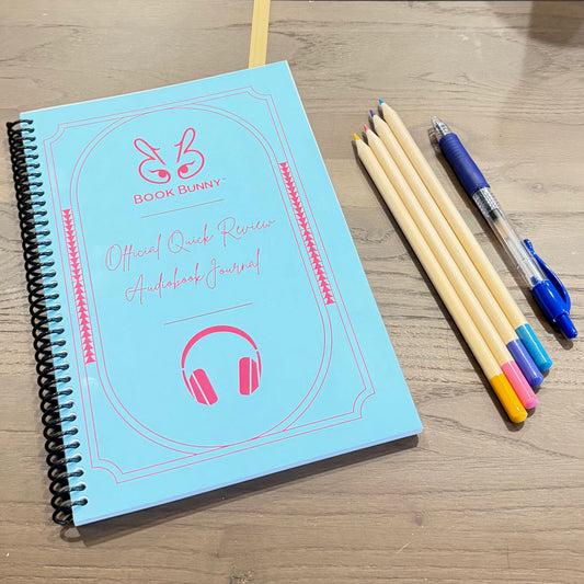 Turquoise coil-bound Book Bunny™ Official Quick Review Audiobook Journal shown with a blue pen and colored pencils.